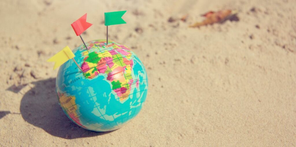 A vibrant globe with pins on a sandy surface, symbolizing travel plans.
